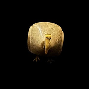 May include: A small, beige, bird-shaped sculpture with a gold beak. The sculpture is made of a smooth, polished material and has a rounded shape.