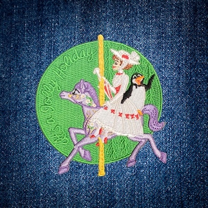 May include: Embroidered patch featuring a carousel scene with a woman, a penguin, and a purple horse. The woman wears a white dress and hat. The patch is on a denim background and includes the text "a Jolly Holiday".