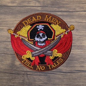 May include: Embroidered patch featuring a pirate skull wearing a tricorn hat with crossed swords. The patch is circular with the words "DEAD MEN TELL NO TALES" in a brown and gold design, with red accents.
