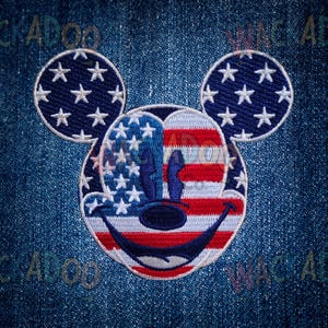 May include: Embroidered patch featuring Mickey Mouse's face with an American flag design. The ears are blue with white stars. The face is divided into red and white stripes and blue with white stars. The patch is on a blue denim background.
