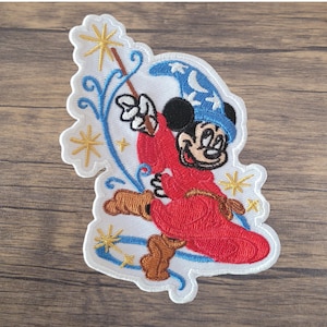 May include: Embroidered patch featuring Mickey Mouse in a red robe and blue wizard hat, holding a wand with a star. The patch has a white border with gold stars and blue swirls, perfect for decorating clothing or accessories.