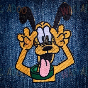 May include: Embroidered patch featuring a cartoon dog with yellow fur, black ears, and a pink tongue. The dog is making a peace sign with both hands. The patch is on a blue denim background.