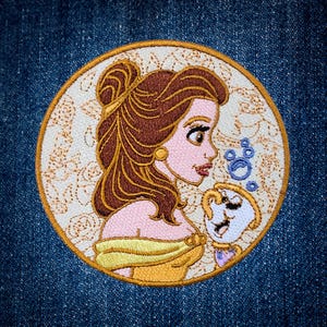 May include: A circular embroidered patch featuring a profile view of a brown-haired character in a yellow off-the-shoulder dress, accompanied by a small white teacup character with blue bubbles, all set against a cream background with gold stitching.