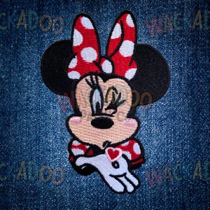 May include: Embroidered Minnie Mouse patch. The design features Minnie with a red and white polka dot bow, black ears, and a red and white polka dot dress. She holds a white glove with a red heart. Set against a blue denim background.