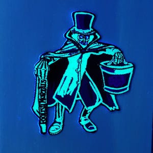 May include: Embroidered patch featuring a skeleton in a top hat and cape, holding a lantern and bucket. The patch has a black and teal color scheme, with the words "Kooky Mortals" on the lantern.