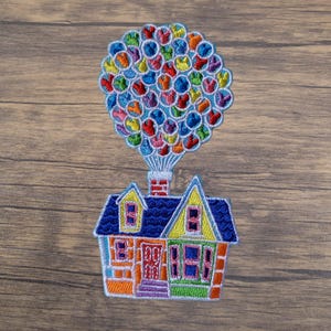 May include: Embroidered patch featuring a colorful house with a blue roof and a cluster of balloons in various colors. The house has yellow and orange accents, with a chimney and a purple front door. The balloons are in a variety of colors.