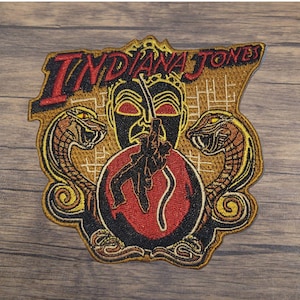 May include: An embroidered patch featuring Indiana Jones with a snake on each side, a skull, and the text "Indiana Jones".