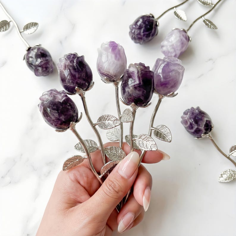 Peut inclure: Sculptures de roses en am&eacute;thyste. Les boutons de rose sont sculpt&eacute;s dans de la pierre violette et blanche, avec des tiges et des feuilles en m&eacute;tal argent&eacute;. Les roses sont dispos&eacute;es en bouquet, avec plusieurs autres &eacute;parpill&eacute;es.