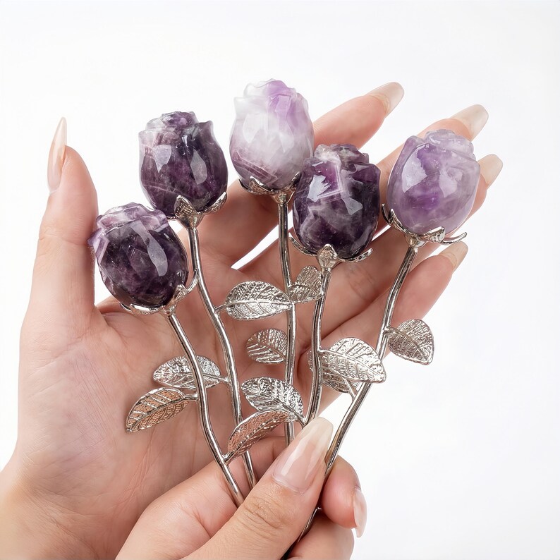 Peut inclure: Un bouquet de cinq sculptures de roses en am&eacute;thyste. Les boutons de rose sont un m&eacute;lange de violet fonc&eacute; et de blanc, avec des tiges et des feuilles argent&eacute;es. Les sculptures sont tenues dans une main sur fond blanc.