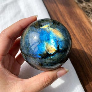 以下が含まれることがあります： 磨かれたラブラドライトの球体で、魅惑的な色の遊びを見せています。球体の表面は鮮やかな青、黄色、緑を反射し、虹色の効果を生み出しています。ユニークな装飾品です。