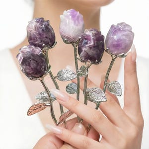 Peut inclure: Cinq sculptures de roses en am&eacute;thyste avec des tiges et des feuilles argent&eacute;es. Les p&eacute;tales de rose sont sculpt&eacute;s dans du cristal violet et blanc. Les tiges sont tenues dans une main.