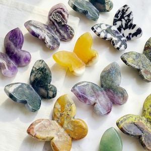 May include: A collection of gemstone butterfly figurines in various colors and patterns. The butterflies are carved from materials like amethyst, yellow quartz, and green stone. The wings display unique veining and textures, creating a natural and artistic aesthetic.