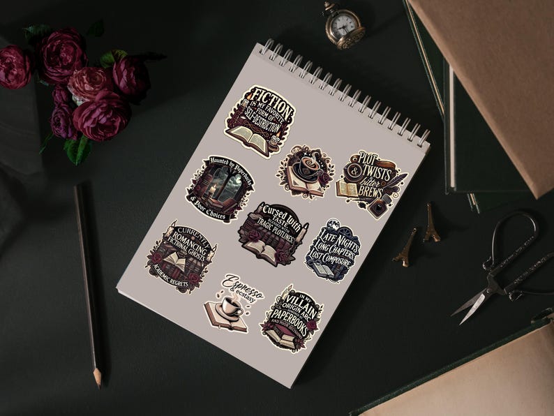 Op de afbeelding: Een verzameling stickers met gotische en literaire thema's. De stickers bevatten zinnen als "Fiction", "Cursed Taste" en "Late Nights". De stickers zijn gerangschikt op een spiraalgebonden notitieboek, met een potlood, bloemen en andere decoratieve items.