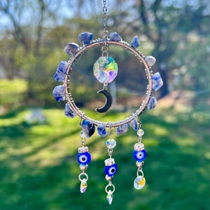 May include: A silver wire dream catcher with blue and white stones, a crescent moon charm, and three evil eye charms hanging from it.