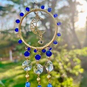 May include: Gold wire hoop with a crescent moon and star charm, blue beads, and crystal prisms hanging from the bottom. The hoop also features a blue evil eye charm.