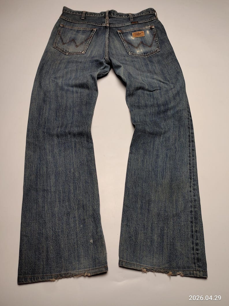 Peut inclure: Jean en denim bleu d&eacute;lav&eacute; avec une conception classique &agrave; cinq poches. Le jean pr&eacute;sente le logo Wrangler sur les poches arri&egrave;re et un aspect us&eacute;, sugg&eacute;rant un style vintage. Le jean est pos&eacute; &agrave; plat, mettant en valeur toute la longueur et les d&eacute;tails.