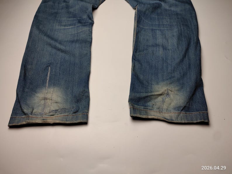 May include: Faded blue denim jeans with a light wash on the lower legs. The jeans have a classic five-pocket design and a straight leg cut. The denim shows signs of wear and tear, adding to the vintage aesthetic.