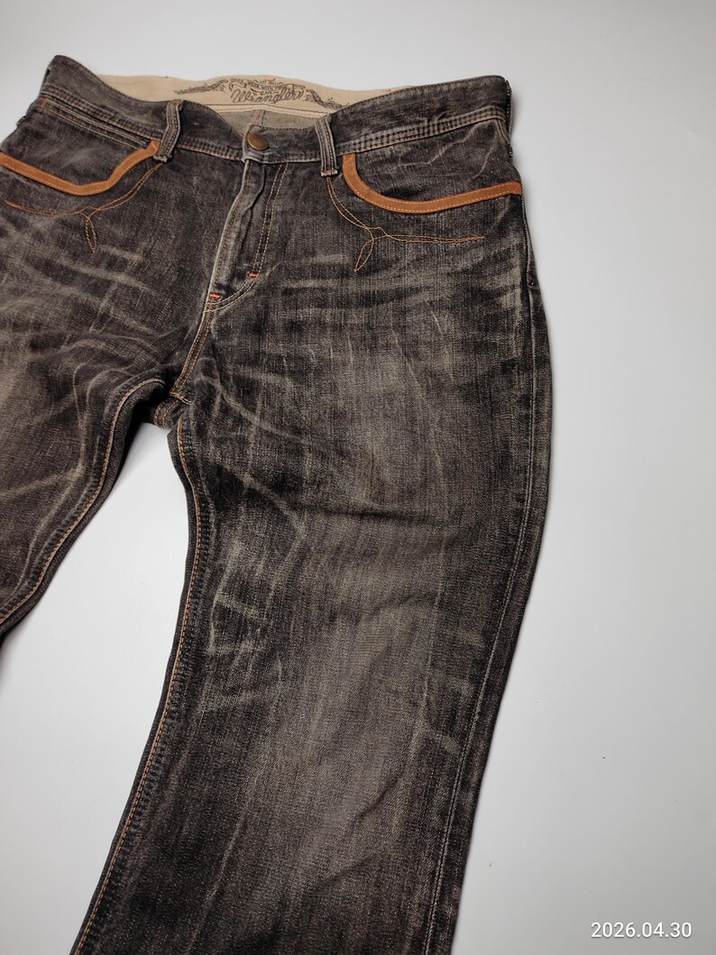 May include: Dark gray denim jeans with brown accents on the pockets and seams. The jeans have a faded, worn look and a classic five-pocket design. The waistband features a printed label.