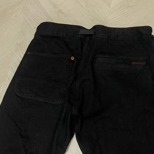 Puede incluir: Pantalones negros con un bolsillo trasero visible y un peque&ntilde;o logotipo rojo. Los pantalones tienen cierre de bot&oacute;n y trabilla para el cintur&oacute;n. La tela parece ser un material resistente, adecuado para actividades al aire libre o ropa casual.