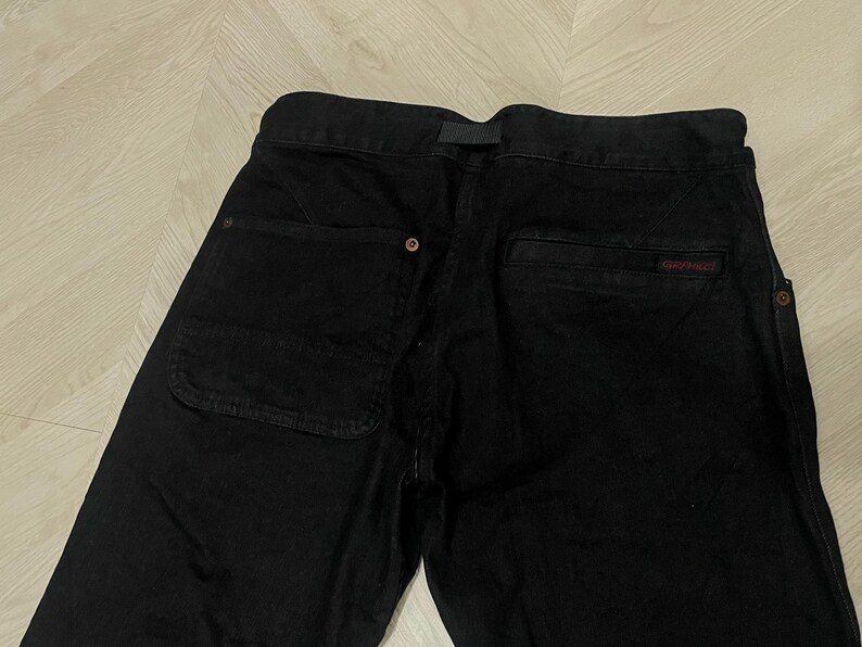 Puede incluir: Pantalones negros con un bolsillo trasero visible y un peque&ntilde;o logotipo rojo. Los pantalones tienen cierre de bot&oacute;n y trabilla para el cintur&oacute;n. La tela parece ser un material resistente, adecuado para actividades al aire libre o ropa casual.