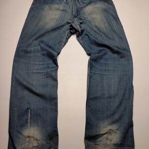May include: Faded blue denim trousers with an elasticated waistband and drawstring. The jeans have a relaxed fit and show signs of wear, with lighter patches on the legs. The back pockets are visible, and the overall style is casual.
