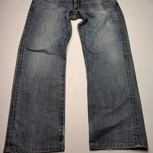 May include: Blue denim jeans with a classic five-pocket design. The jeans have a faded wash and a straight leg cut. The image shows the jeans laid flat on a white surface, showcasing the front and back details.