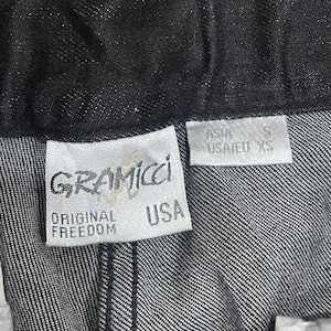Puede incluir: Primer plano de unos pantalones vaqueros oscuros. La etiqueta de la marca Gramicci es visible, con las palabras "ORIGINAL FREEDOM" y "USA" impresas. La etiqueta de talla indica "USA/EU XS" y "ASIA S".
