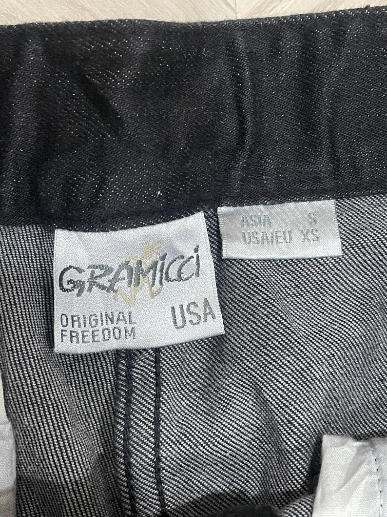 Puede incluir: Primer plano de unos pantalones vaqueros oscuros. La etiqueta de la marca Gramicci es visible, con las palabras "ORIGINAL FREEDOM" y "USA" impresas. La etiqueta de talla indica "USA/EU XS" y "ASIA S".