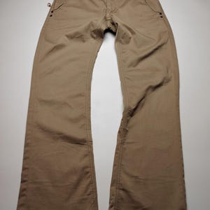 May include: Khaki-colored pants with a classic five-pocket design. The pants have a button closure and a zipper fly. The stitching is visible along the seams and pockets. The pants are made of a durable fabric and have a straight leg cut.