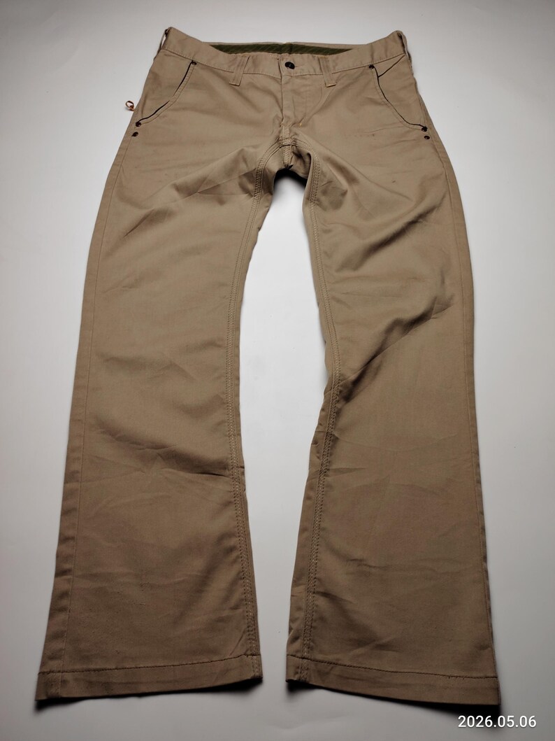 May include: Khaki-colored pants with a classic five-pocket design. The pants have a button closure and a zipper fly. The stitching is visible along the seams and pockets. The pants are made of a durable fabric and have a straight leg cut.