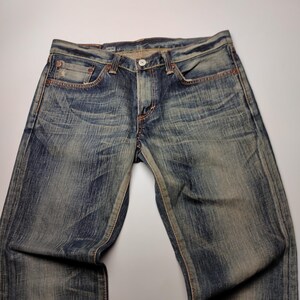 May include: Faded blue denim jeans with a classic five-pocket design. The jeans have a button closure and a worn, distressed look. The denim is a medium wash with subtle fading and whiskering.