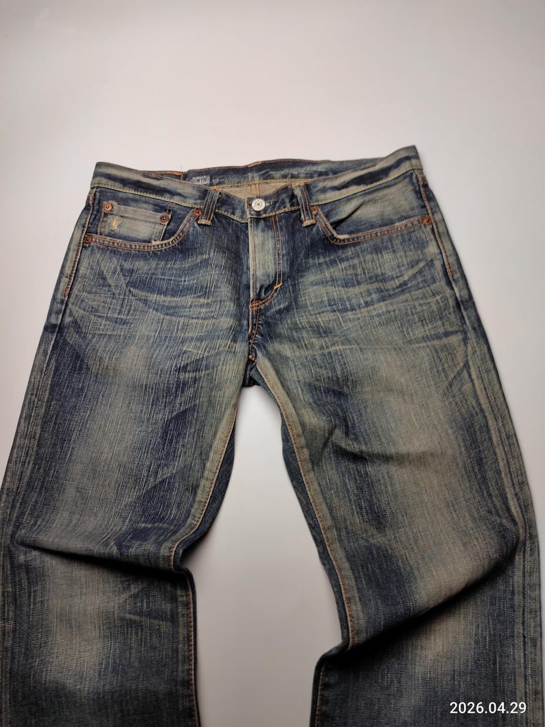 May include: Faded blue denim jeans with a classic five-pocket design. The jeans have a button closure and a worn, distressed look. The denim is a medium wash with subtle fading and whiskering.