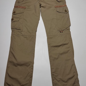 May include: Khaki-colored cargo pants with multiple pockets and button closures. The pants have a relaxed fit and feature reinforced details at the pockets. The design includes a button and zipper fly, and a brown accent on the pockets.
