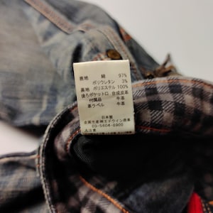 Puede incluir: Primer plano de una chaqueta vaquera con forro de cuadros visible. La chaqueta tiene costuras visibles y una etiqueta con texto japon&eacute;s. La etiqueta enumera los materiales: algod&oacute;n, poliuretano y poli&eacute;ster.