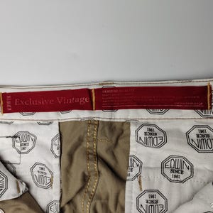 May include: Close-up of the inside of a pair of khaki-colored pants. The interior lining is white with a repeating black and white octagonal pattern that reads "EDWIN SINCE 1961". A red tag reads "Exclusive Vintage".