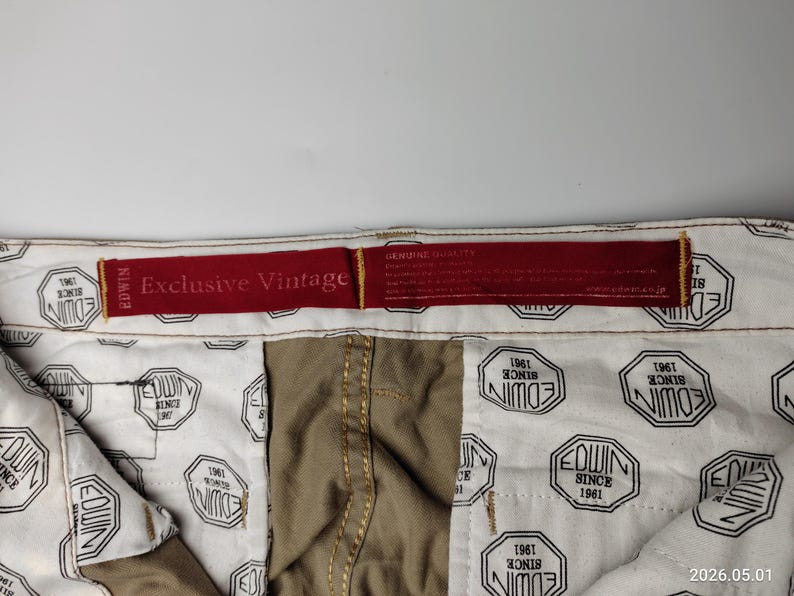 May include: Close-up of the inside of a pair of khaki-colored pants. The interior lining is white with a repeating black and white octagonal pattern that reads "EDWIN SINCE 1961". A red tag reads "Exclusive Vintage".