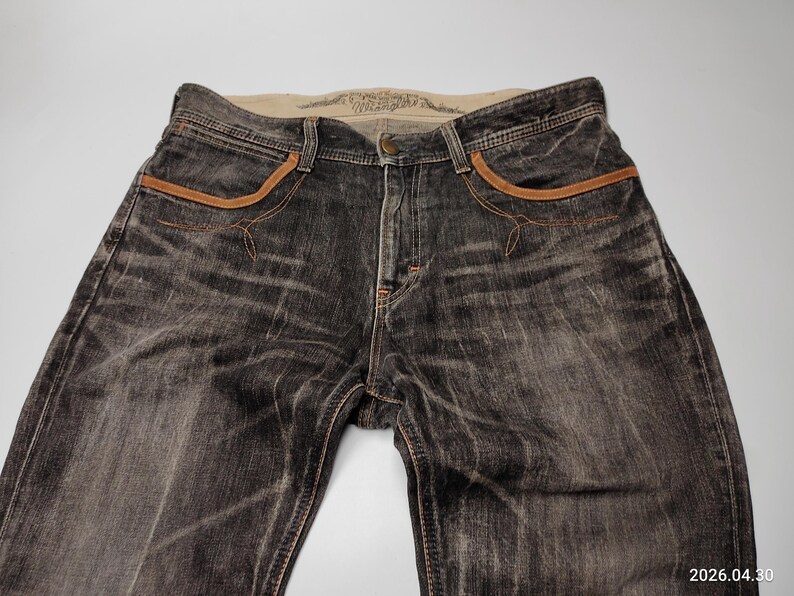 May include: Faded black denim jeans with brown pocket trim and stitching. The jeans have a classic five-pocket design and a button closure. The denim has a worn, distressed look.