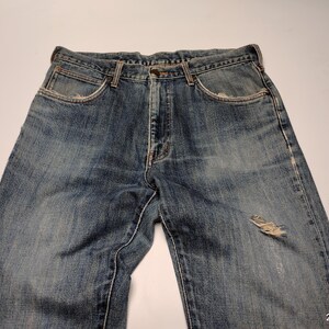 Peut inclure: Jean bleu d&eacute;lav&eacute; avec un aspect us&eacute;. Le jean a une conception classique &agrave; cinq poches, une fermeture &agrave; bouton et &agrave; glissi&egrave;re, et une pi&egrave;ce us&eacute;e sur le genou. Le denim a un lavage vintage avec une d&eacute;coloration et une usure subtiles.
