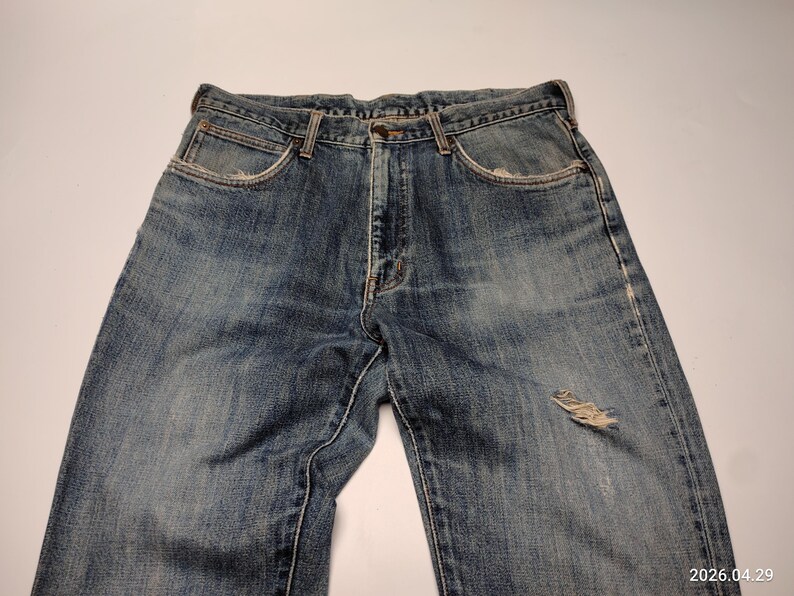 Peut inclure: Jean bleu d&eacute;lav&eacute; avec un aspect us&eacute;. Le jean a une conception classique &agrave; cinq poches, une fermeture &agrave; bouton et &agrave; glissi&egrave;re, et une pi&egrave;ce us&eacute;e sur le genou. Le denim a un lavage vintage avec une d&eacute;coloration et une usure subtiles.