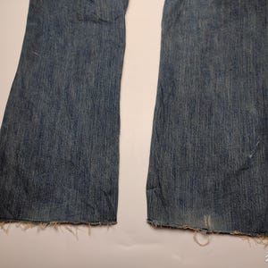 May include: Close-up of a pair of blue denim jeans with a flared leg design. The jeans have a distressed look with frayed edges at the hem. The denim is a medium wash with subtle fading.