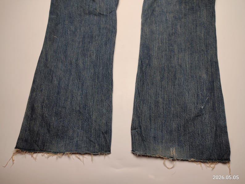 May include: Close-up of a pair of blue denim jeans with a flared leg design. The jeans have a distressed look with frayed edges at the hem. The denim is a medium wash with subtle fading.
