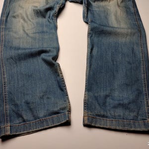 May include: Faded blue denim jeans with a wide leg cut. The jeans show signs of wear and fading, with visible stitching along the seams and hem. The denim has a vintage, worn-in appearance.