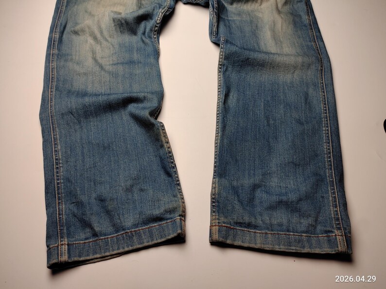 May include: Faded blue denim jeans with a wide leg cut. The jeans show signs of wear and fading, with visible stitching along the seams and hem. The denim has a vintage, worn-in appearance.