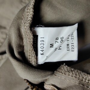 May include: Close-up of a tan garment tag with the text "K40391", "M", "W 78", and "H 96". Additional text includes "ERM-1514" and "E231-2201". The tag is attached to a tan fabric.