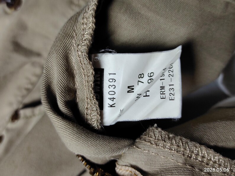 May include: Close-up of a tan garment tag with the text "K40391", "M", "W 78", and "H 96". Additional text includes "ERM-1514" and "E231-2201". The tag is attached to a tan fabric.
