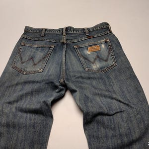 Peut inclure: Jean en denim bleu d&eacute;lav&eacute; avec une coupe classique &agrave; cinq poches. Le logo Wrangler est visible sur les poches arri&egrave;re et une &eacute;tiquette en cuir. Le jean pr&eacute;sente un aspect us&eacute; avec des d&eacute;tails us&eacute;s.