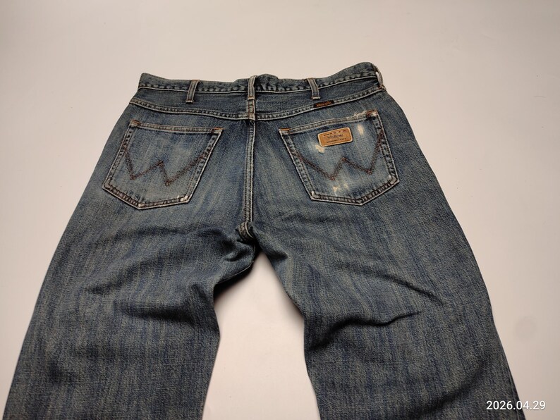 Peut inclure: Jean en denim bleu d&eacute;lav&eacute; avec une coupe classique &agrave; cinq poches. Le logo Wrangler est visible sur les poches arri&egrave;re et une &eacute;tiquette en cuir. Le jean pr&eacute;sente un aspect us&eacute; avec des d&eacute;tails us&eacute;s.