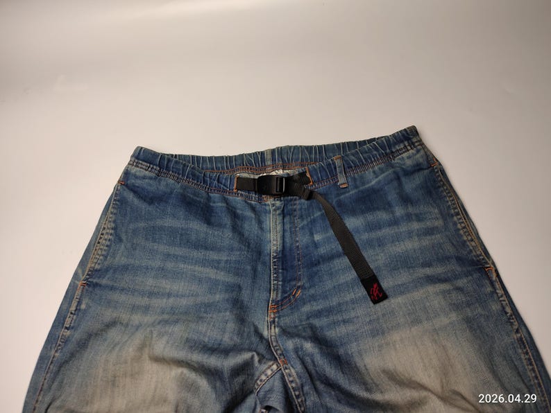 May include: Blue denim trousers with a black belt. The trousers have a faded wash and a relaxed fit. The belt is made of a durable fabric and features a black buckle. The trousers are a casual style.