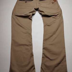 May include: Tan-colored pants with a classic five-pocket design. The back pockets feature black zippers and decorative stitching. The pants are made of a durable fabric and have a straight leg cut.