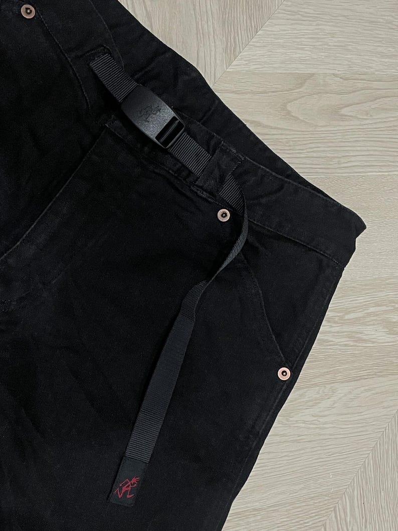 Puede incluir: Pantalones negros con cintur&oacute;n negro incorporado y una peque&ntilde;a etiqueta con el logotipo rojo. Los pantalones tienen un dise&ntilde;o de pierna recta y cuentan con remaches de color cobre. El cintur&oacute;n tiene una hebilla negra. Los pantalones est&aacute;n hechos de tela duradera.